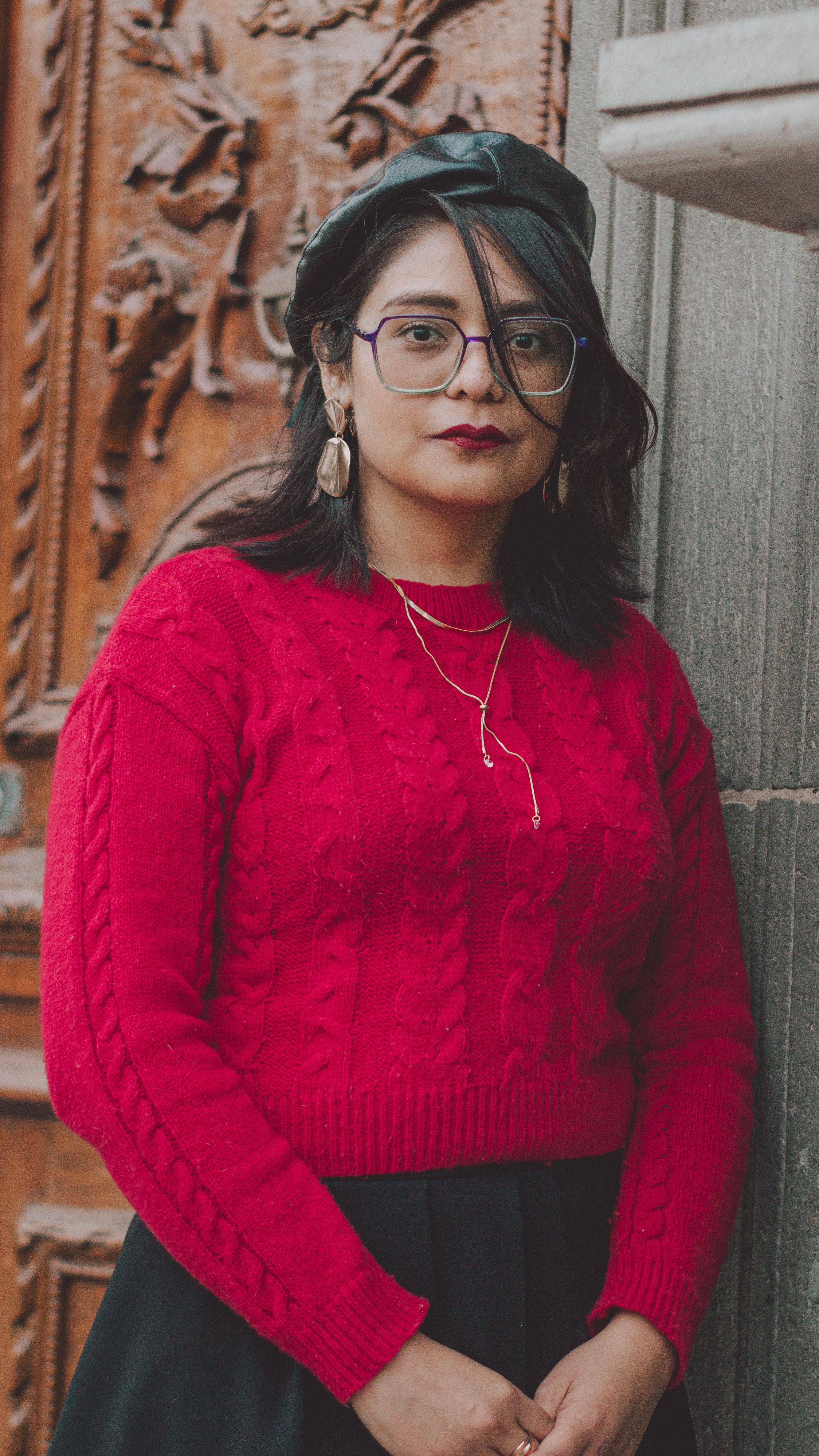 Stylish woman in red sweater with beret and glasses against carved wooden door.