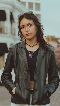 Fashionable woman in leather jacket poses confidently outdoors, urban setting, trendy look.