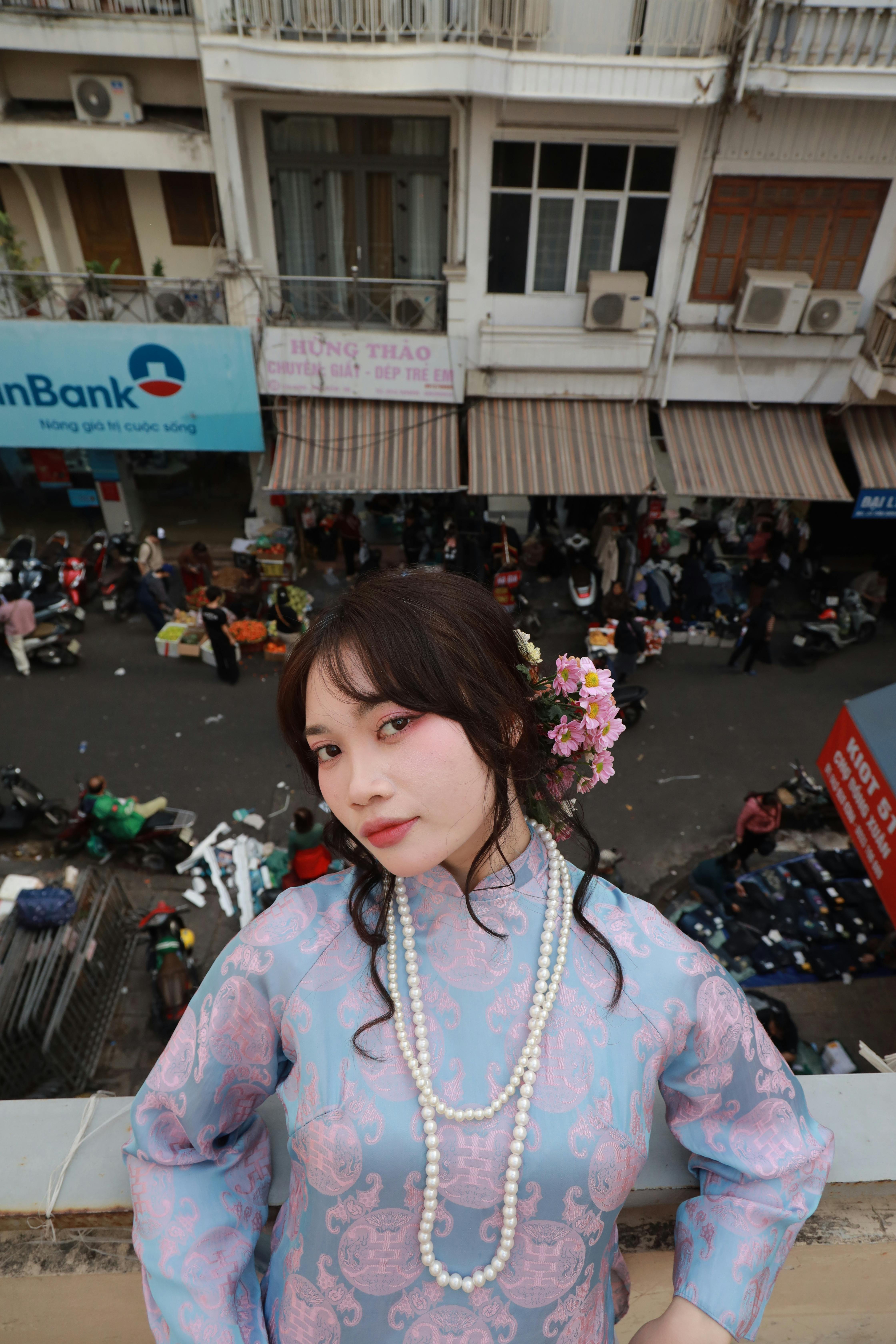 Young woman in traditional dress stands on balcony overlooking a busy street.