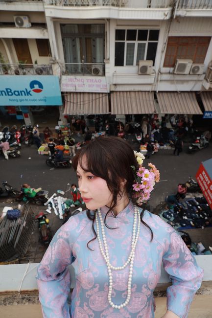 Asian woman in traditional dress with flowers in urban setting, street market below.