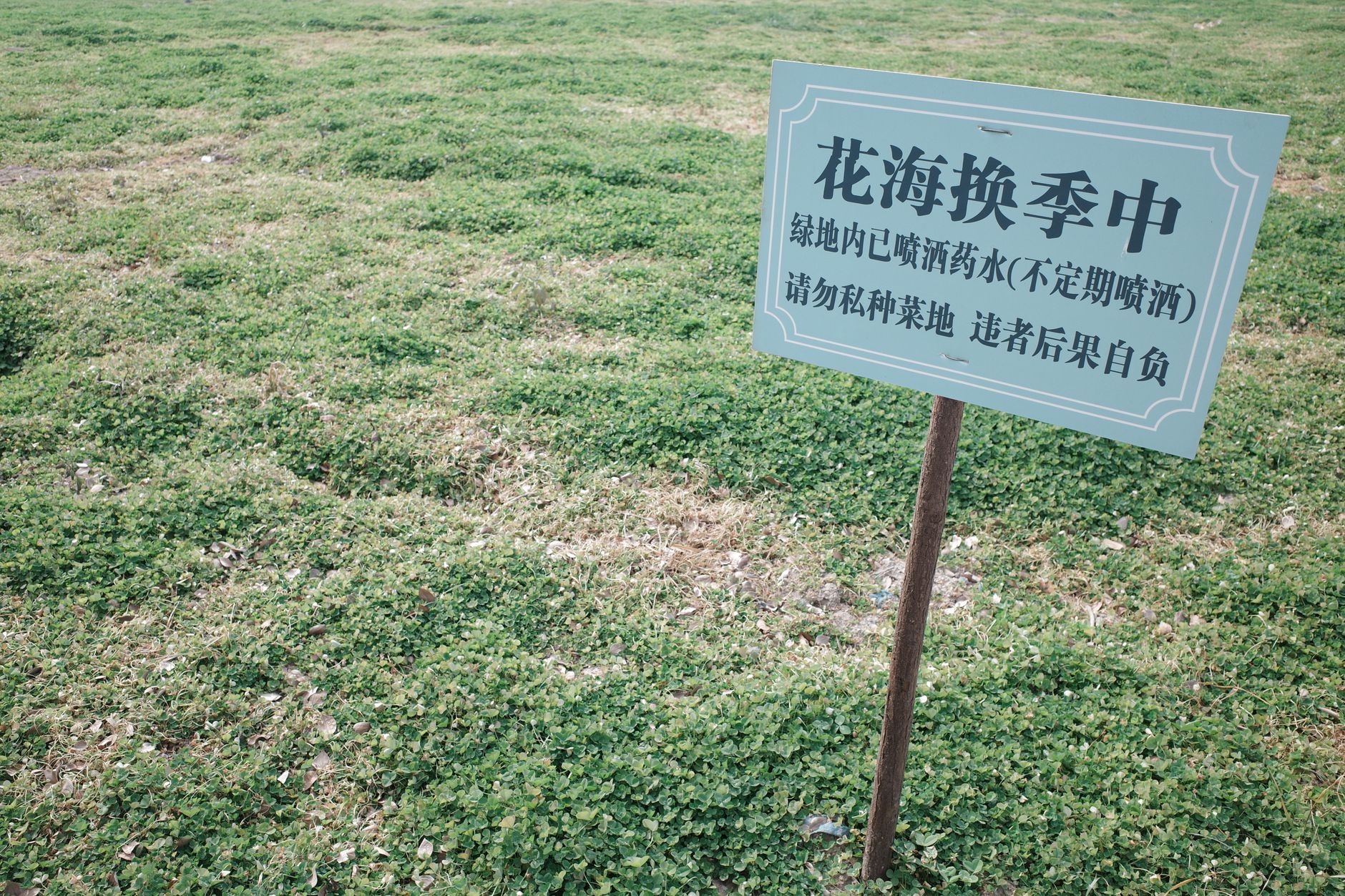 A green field with a sign in Chinese warning of pesticide use.
