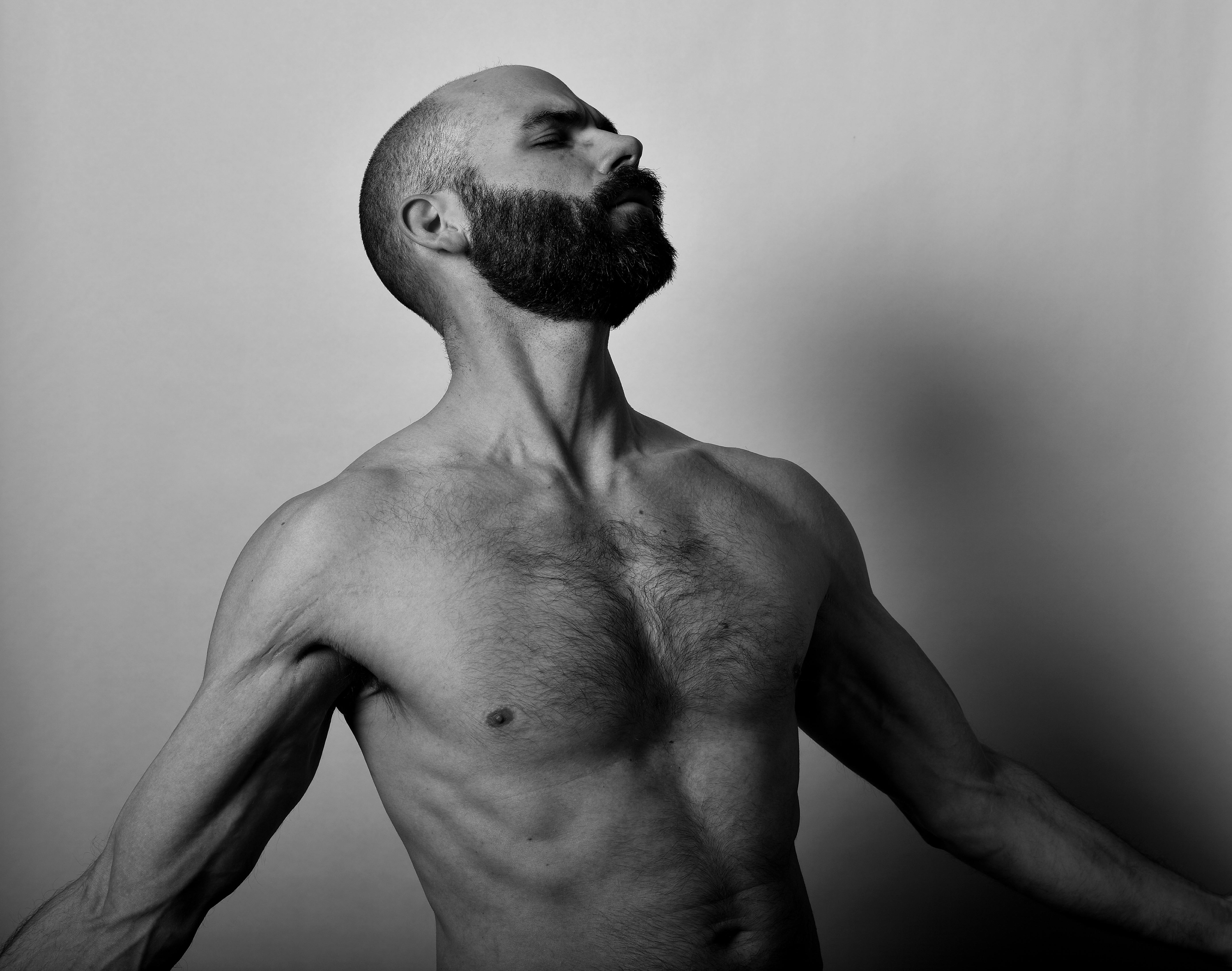 Artistic black and white portrait of a shirtless bearded man with a contemplative expression.