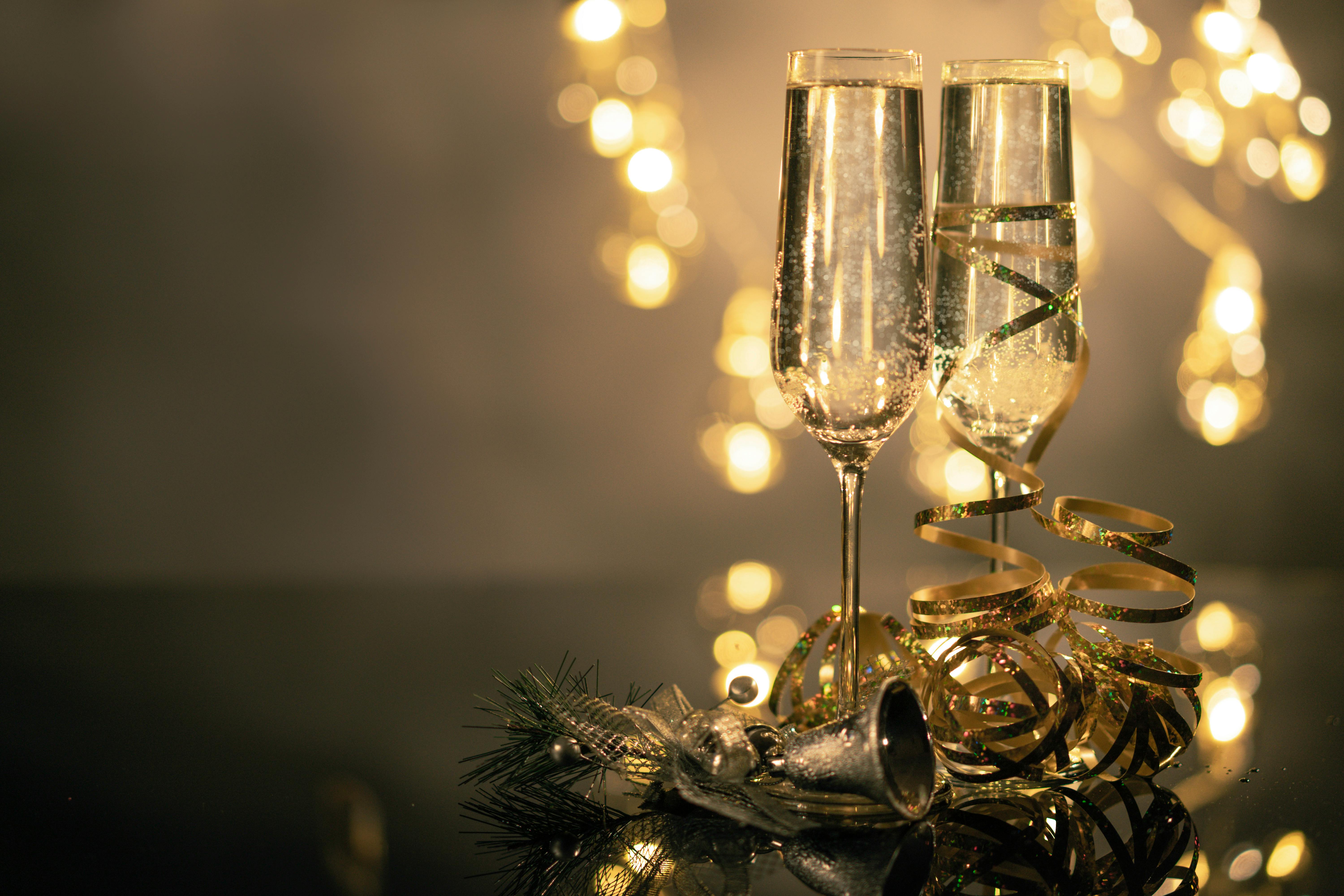 close up of two flute glasses filled with sparkling wine wuth ribbons and christmas decor