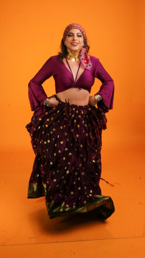 Free Woman in colorful Indian traditional outfit poses joyfully on an orange backdrop. Stock Photo