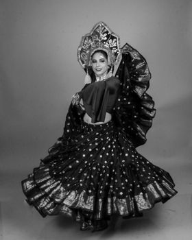 Portrait of a woman in traditional dance attire performing elegantly in a studio setting.