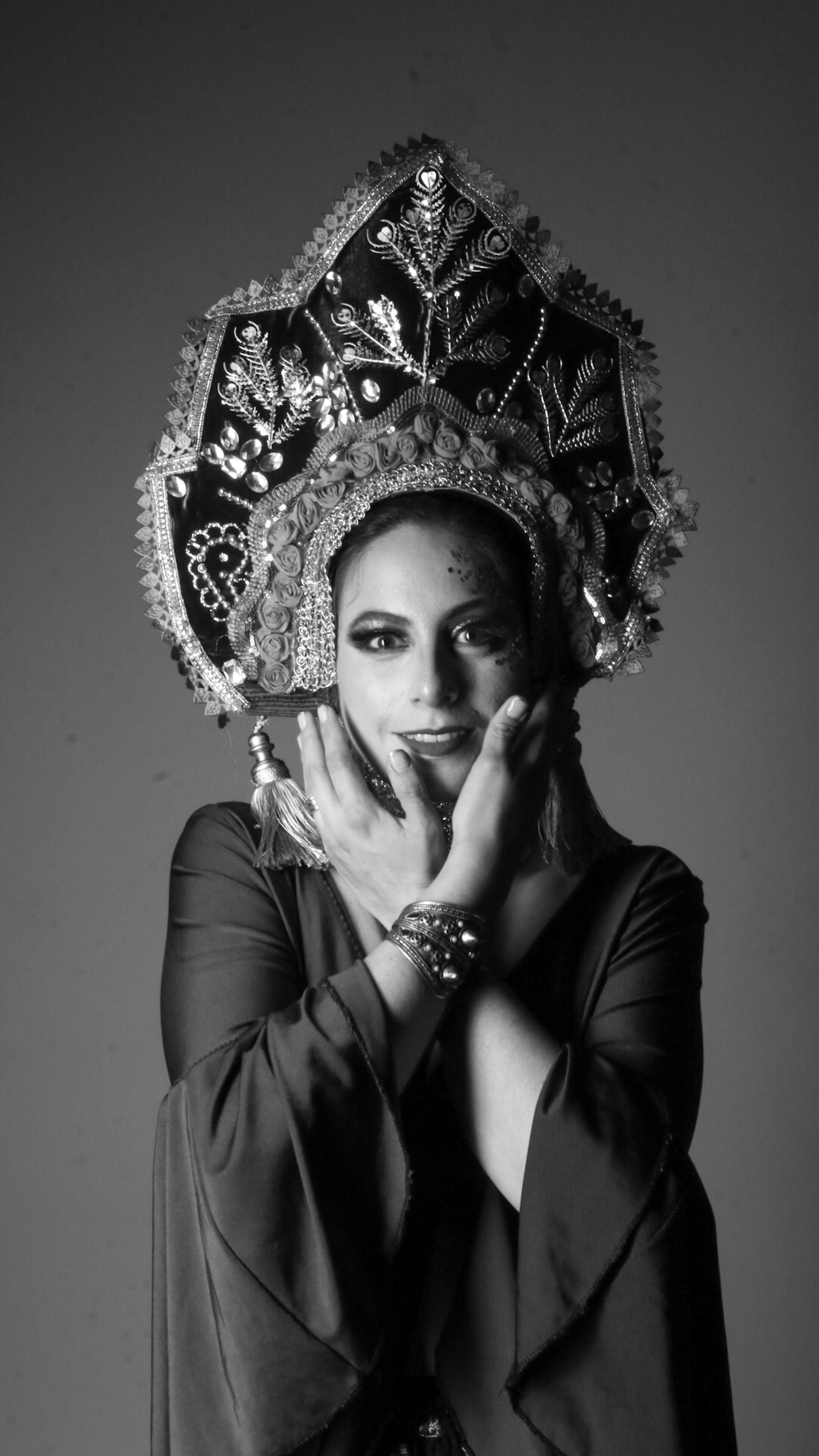 Black and white portrait of a woman in ornate traditional headgear, gracefully posing.