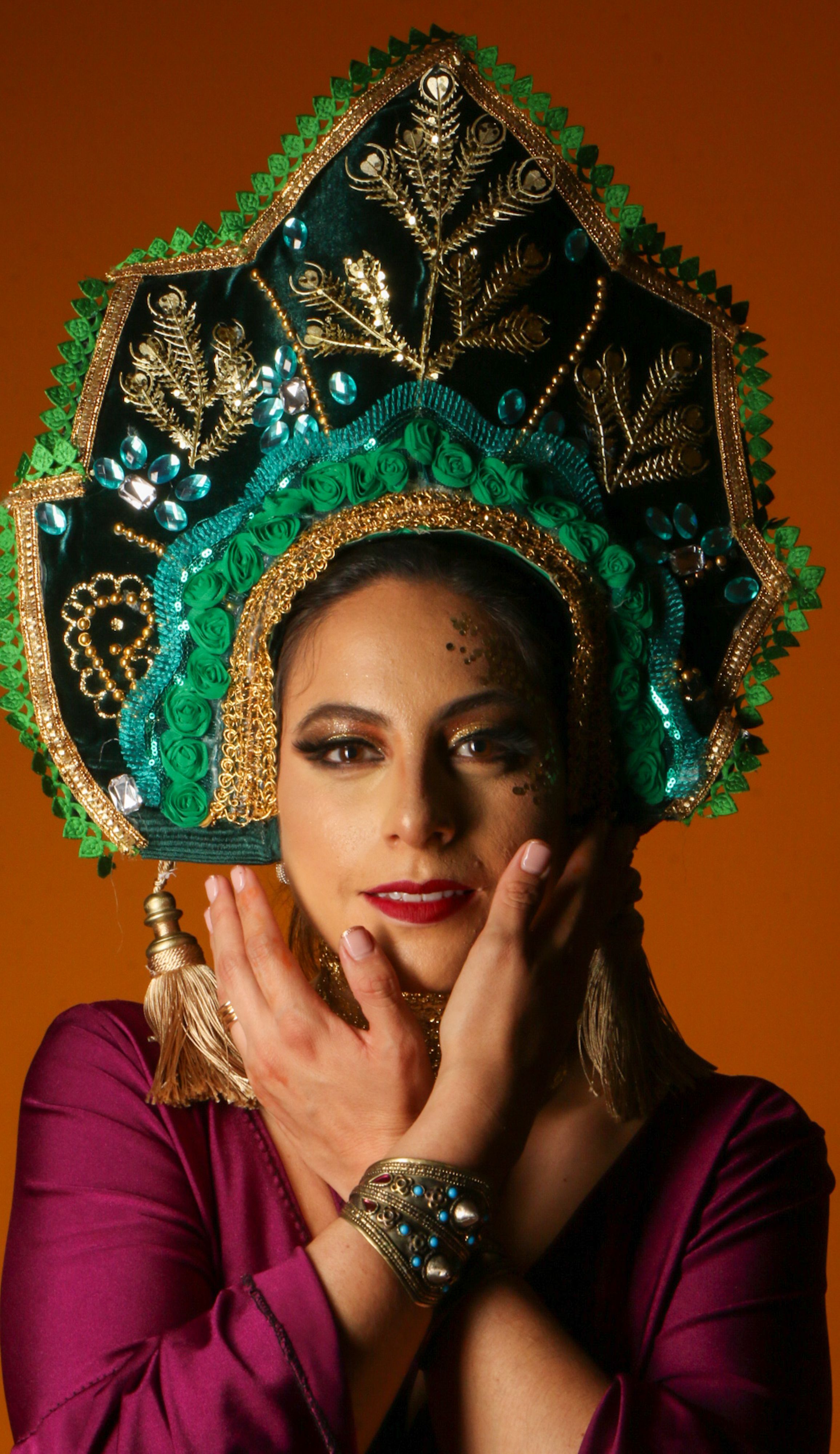 Captivating portrait of a woman wearing an ornate traditional headdress against an orange background.