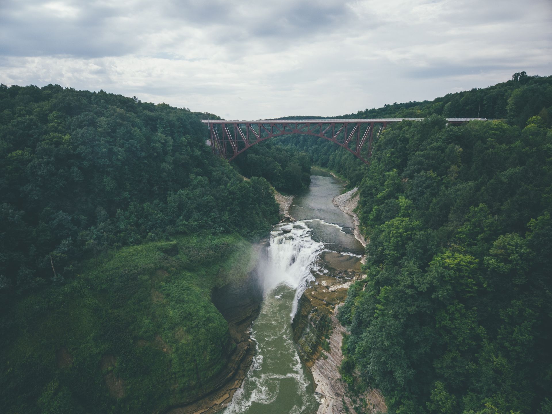 Un pont au-dessus d'un canyon boisé sous un ciel couvert le matin.