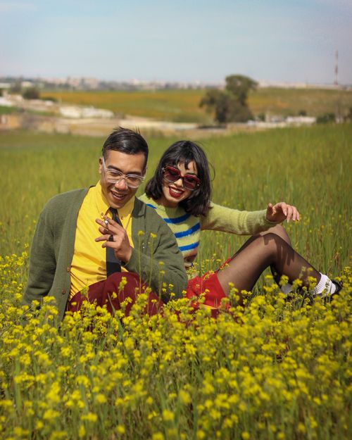 Free Stylish couple enjoying a sunny day in Bouskoura's vibrant yellow flower field, showcasing retro fashion. Stock Photo