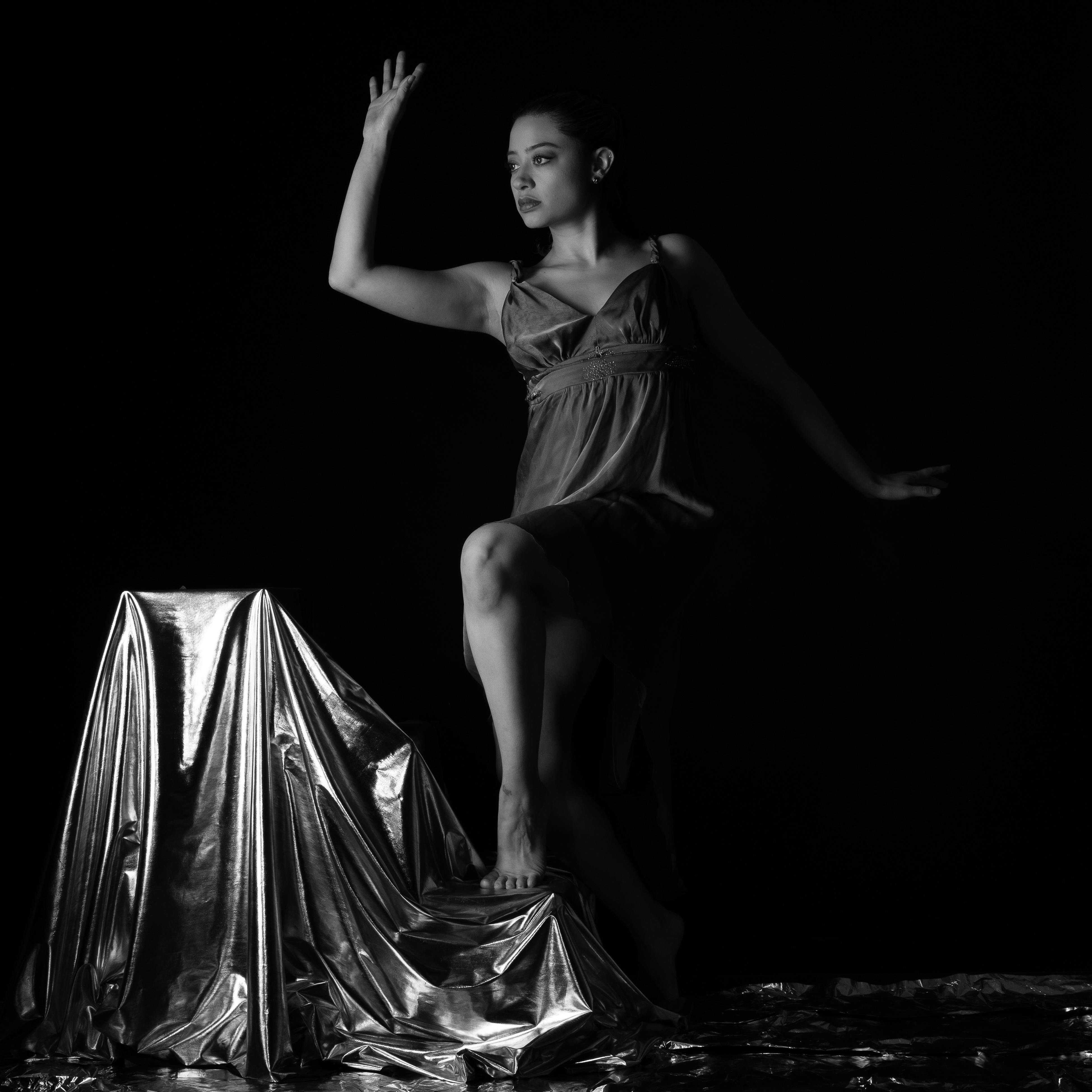 A contemporary dancer poses gracefully against a metallic backdrop in a dramatic black and white portrait.