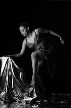 A contemporary dancer gracefully poses with a metallic fabric in a black and white setting.