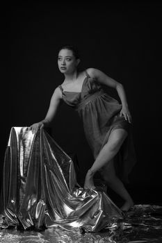 A contemporary dancer poses gracefully in a studio setting with metallic fabric, exuding elegance.