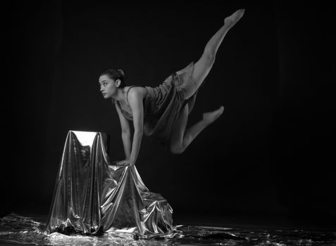 A graceful ballerina in a striking pose with metallic fabrics in black and white.