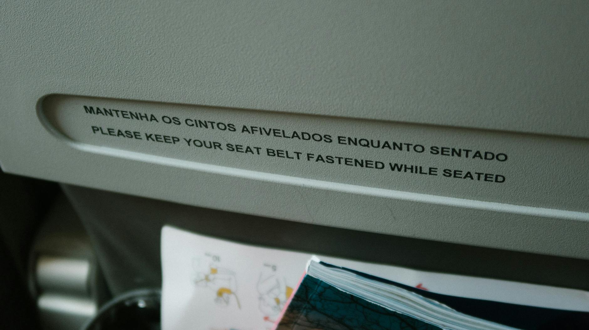 Close-up of an airplane seatback pocket with a seat belt safety message in English and Portuguese.