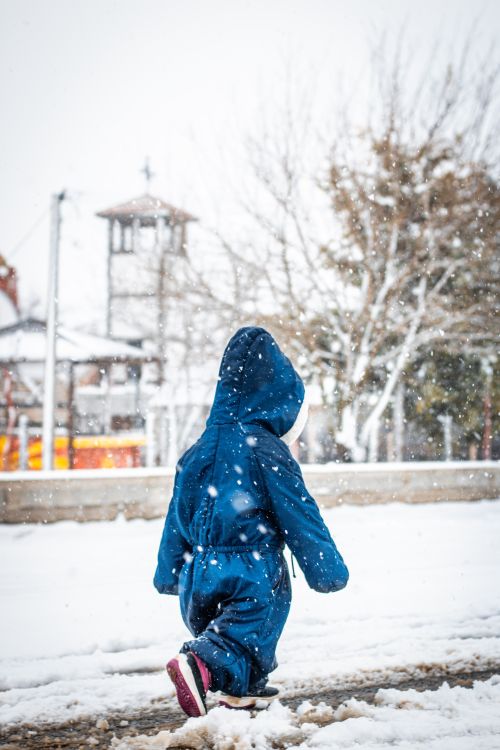 Free A child in a blue snowsuit playing outside during a winter snowfall in North Macedonia. Stock Photo