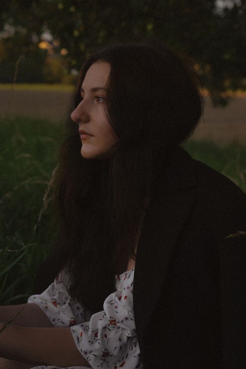 Free A woman pondering in a serene outdoor setting surrounded by nature during twilight. Stock Photo