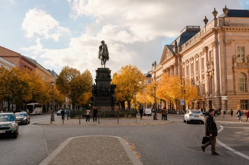 Free Autumn scene of a historical street in Berlin with a prominent statue surrounded by fall foliage. Stock Photo