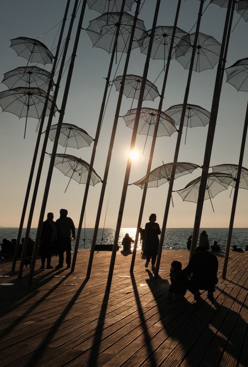 Free Silhouetted people and umbrellas at sunset on the Thessaloniki waterfront. Stock Photo