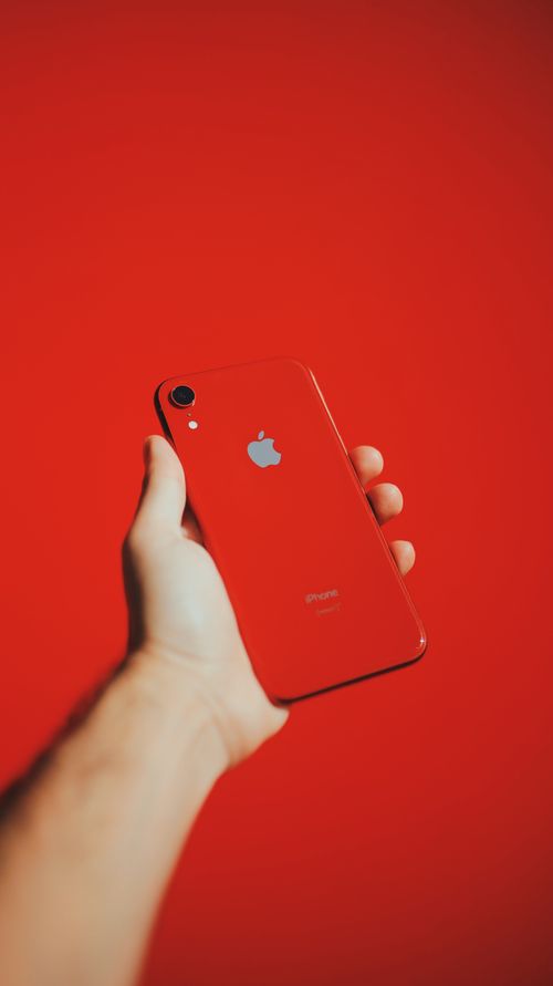 Free A hand holding a sleek red smartphone with a vibrant red background, highlighting modern technology. Stock Photo
