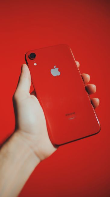 A red smartphone held in a hand against a matching red background, emphasizing modern technology.