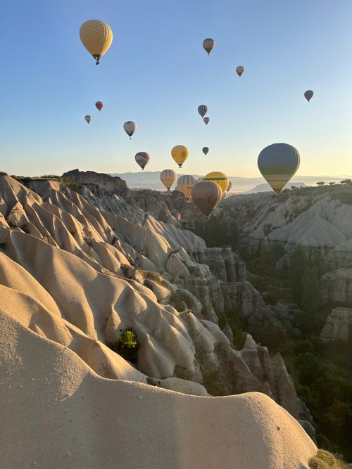 Free Scenic view of hot air balloons floating above Cappadocia's unique landscape at sunrise. Stock Photo