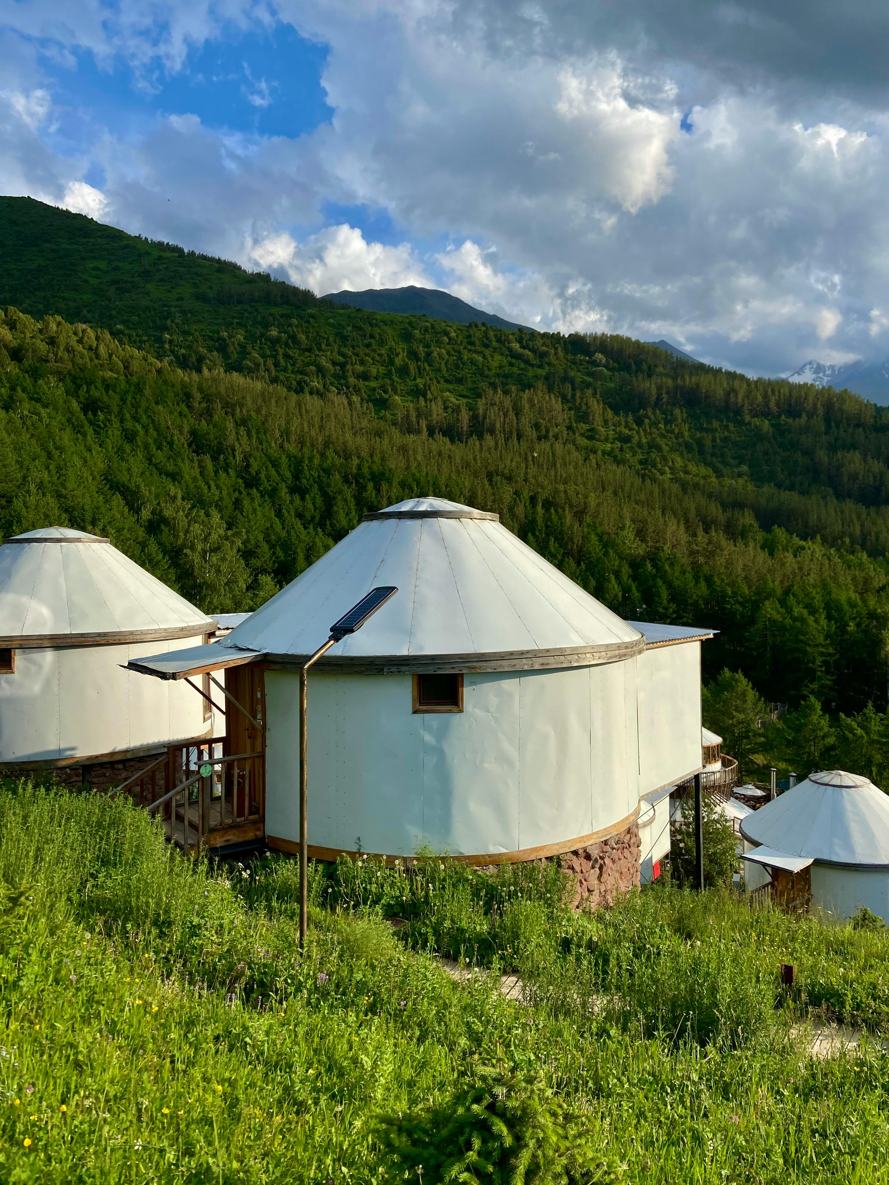 Circular yurts nestled in lush green hills under a cloudy sky.