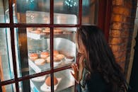 一个女人正透过面包店的窗户，专心地凝视着各式各样的美味糕点