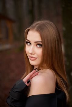 A beautiful woman with long brown hair poses with a smile in an outdoor setting.