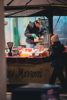 A street vendor prepares roasted chestnuts at an outdoor market stall during the evening.