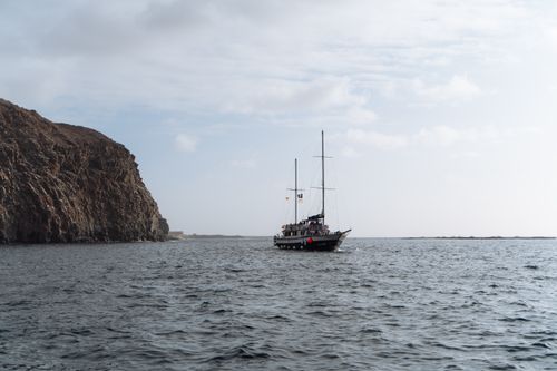 Free Sailing ship cruising near rocky cliffs in clear Tenerife waters, a picturesque maritime adventure. Stock Photo