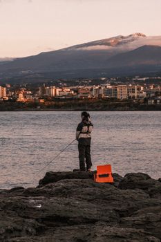 Person fishing by the water with mountains in the background during sunset.