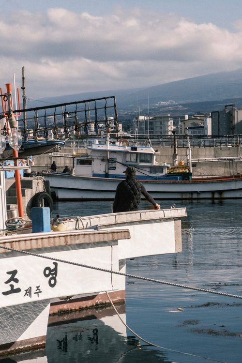 Free A serene harbor scene featuring fishing boats and a distant mountain under a cloudy sky. Stock Photo