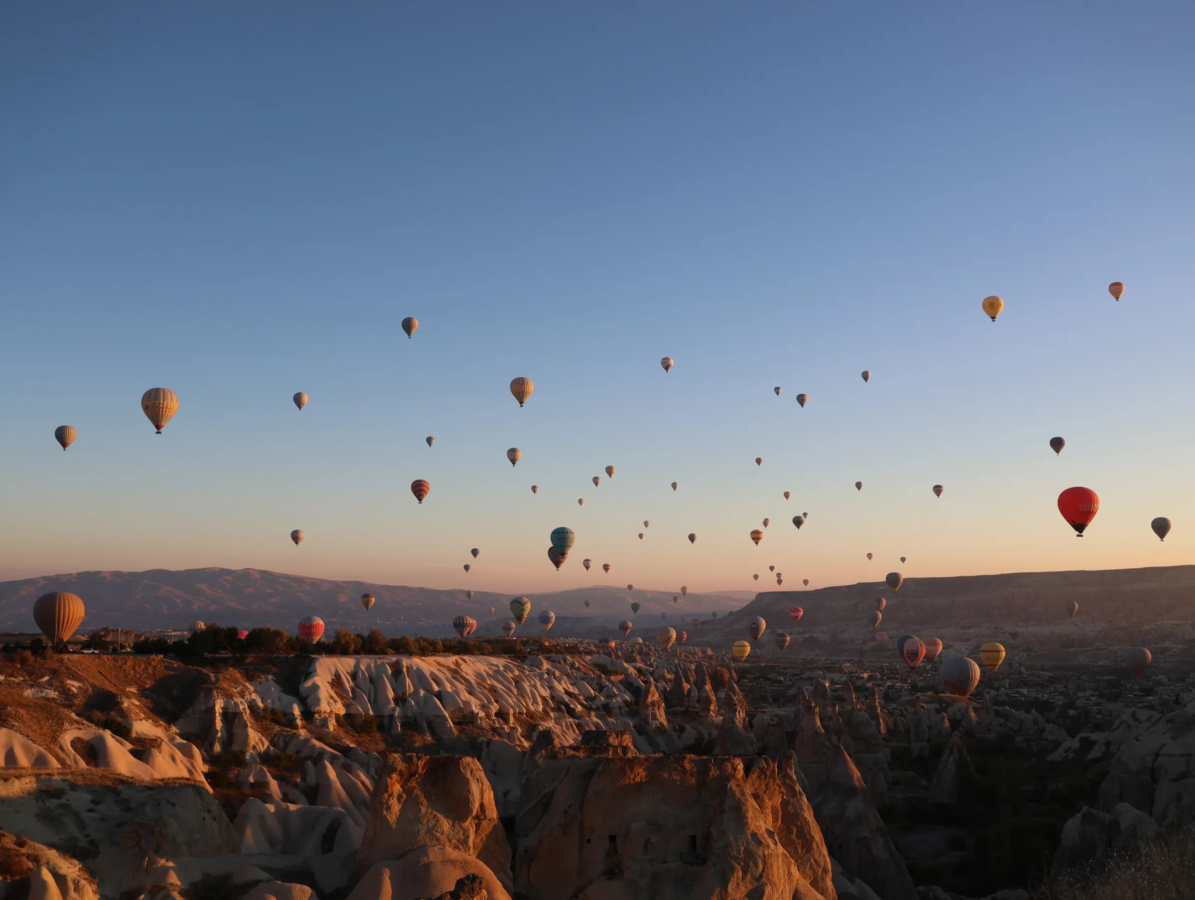 Puluhan balon udara terbang di atas formasi batu Cappadocia, Türkiye, saat langit mulai terang