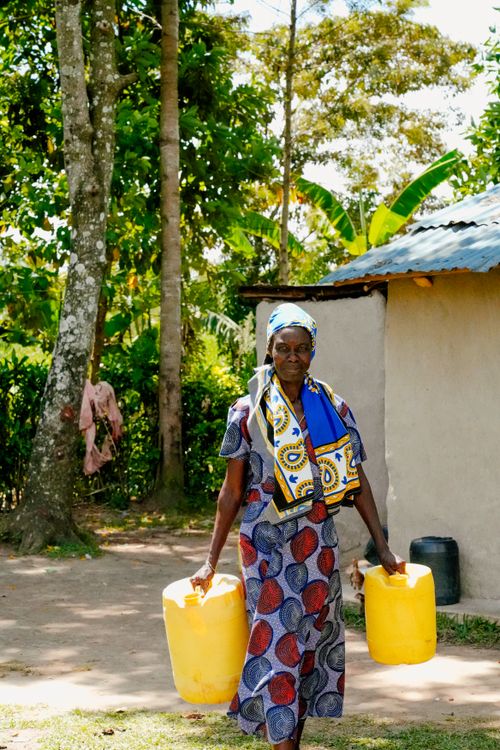 Free An African woman carrying yellow water containers outside in a rural setting. Stock Photo