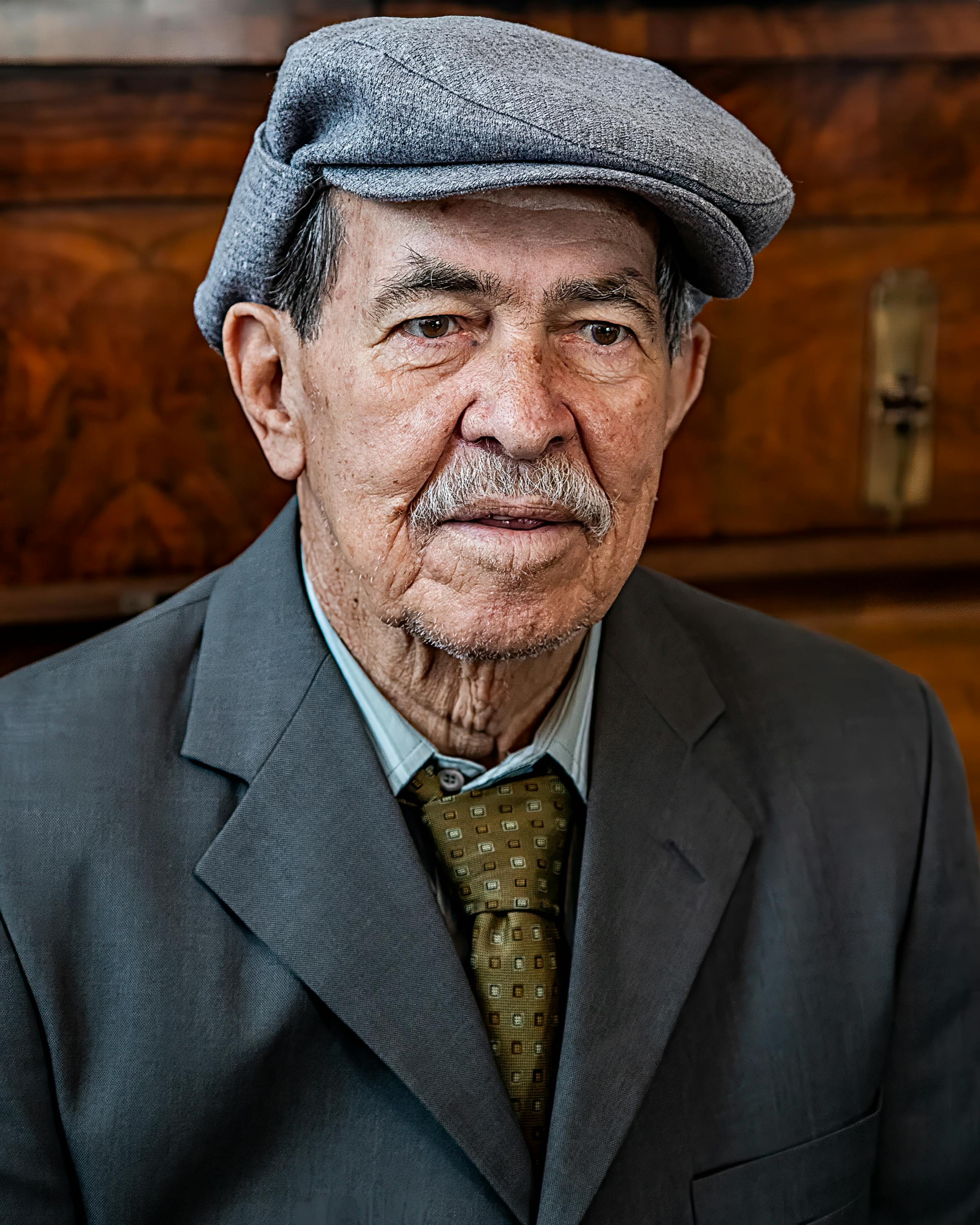 Portrait of an elderly man wearing a gray suit and cap.