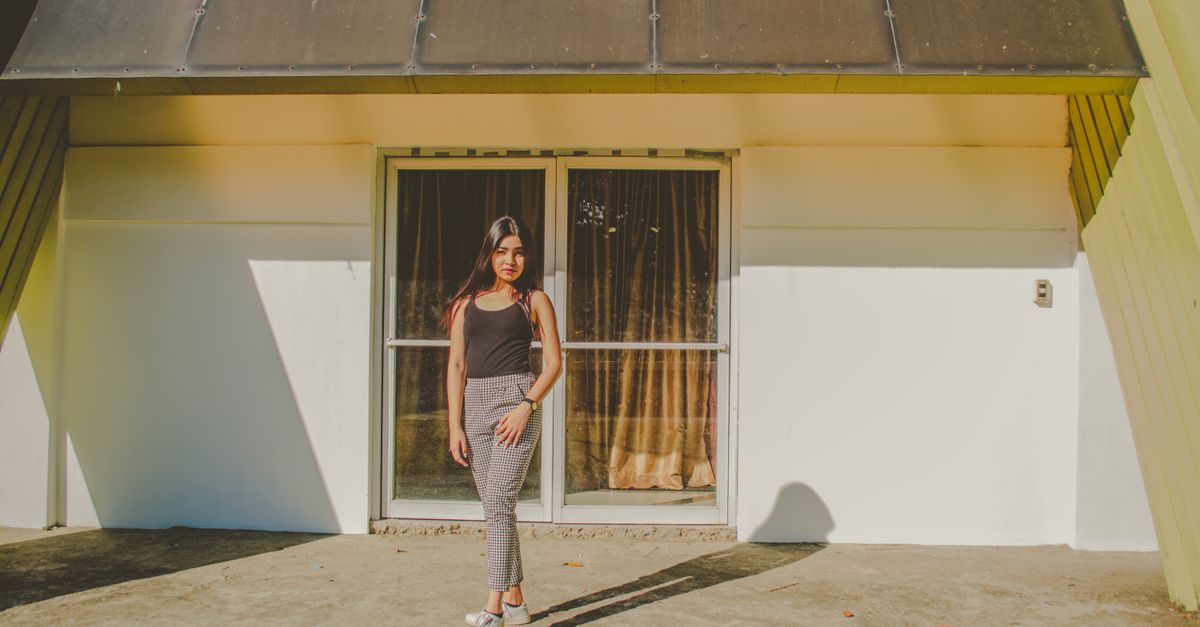 A woman standing in front of a modern house with large glass doors in daylight.