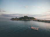 日落时分，海滨宁静，帆船停泊在郁郁葱葱的岛屿附近，展现出一片自然之美