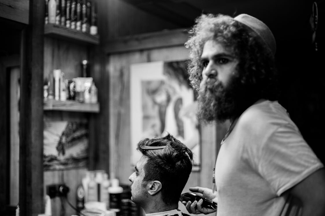 Grayscale Photography of Man Cutting Hair on Seated Man