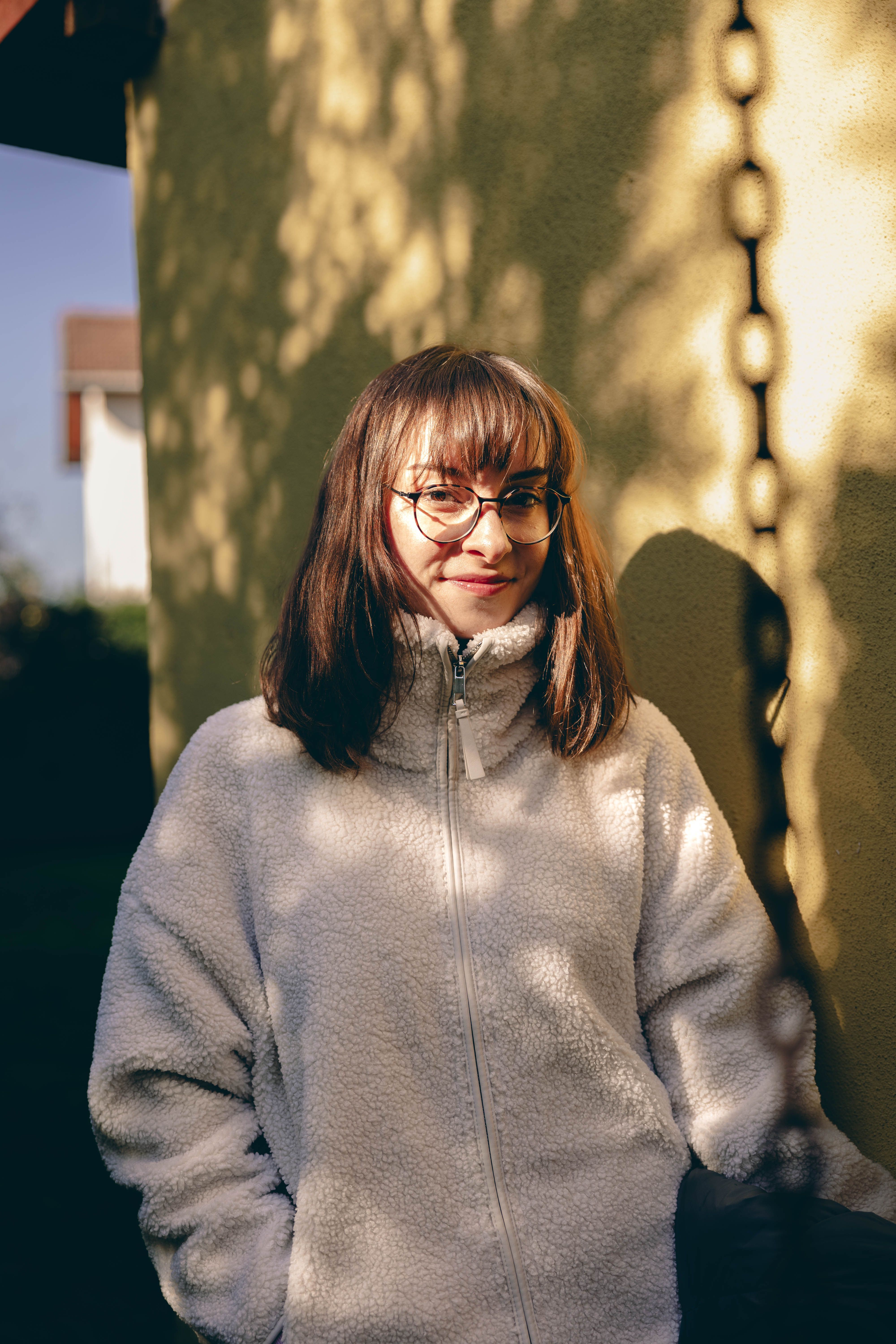 A young woman in a cozy jacket enjoys the sunlight in a garden in İstanbul.