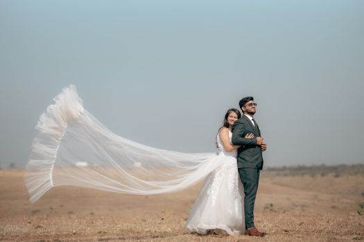 Elegant couple in outdoor pre-wedding photoshoot with flowing veil.