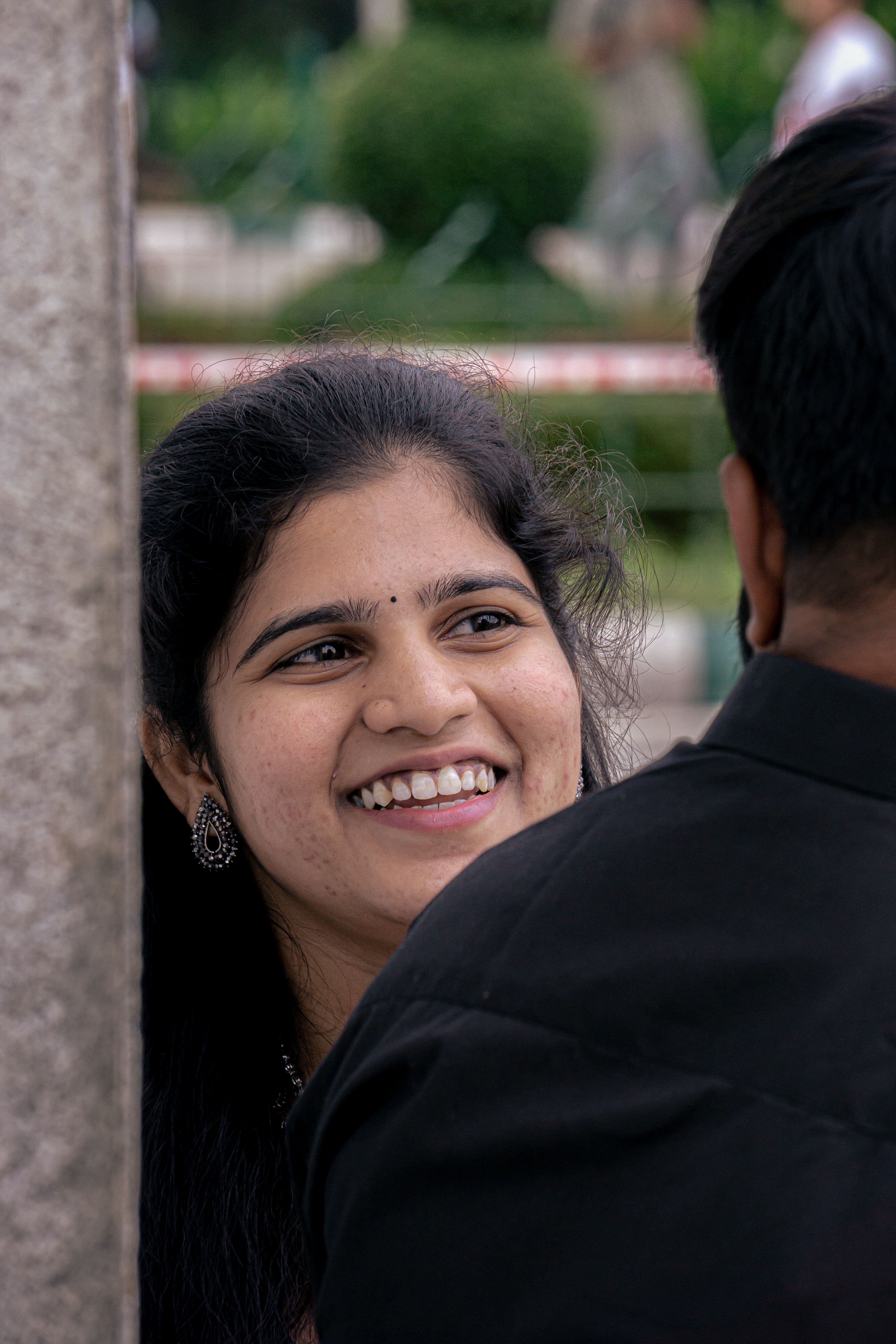A young woman smiling warmly while engaged in a lively conversation outdoors.