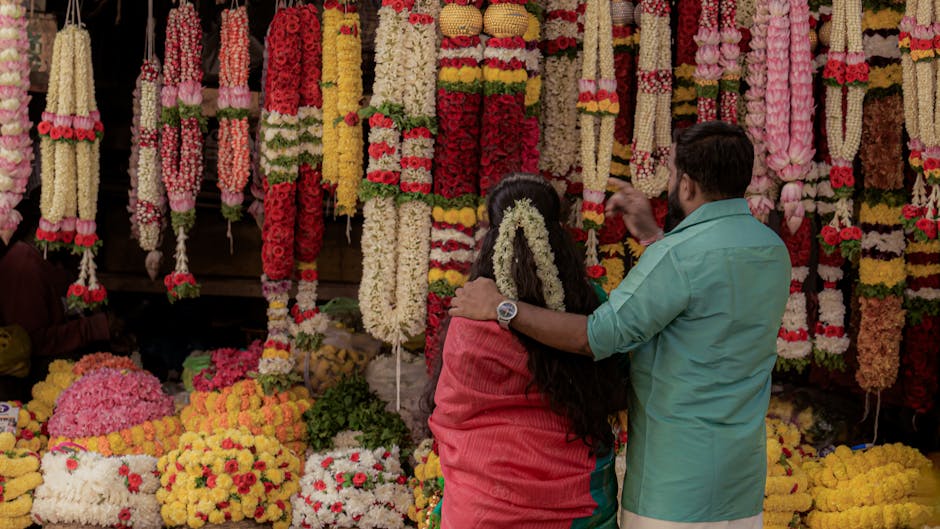 Two people explore a vibrant flower market adorned with intricate garlands.