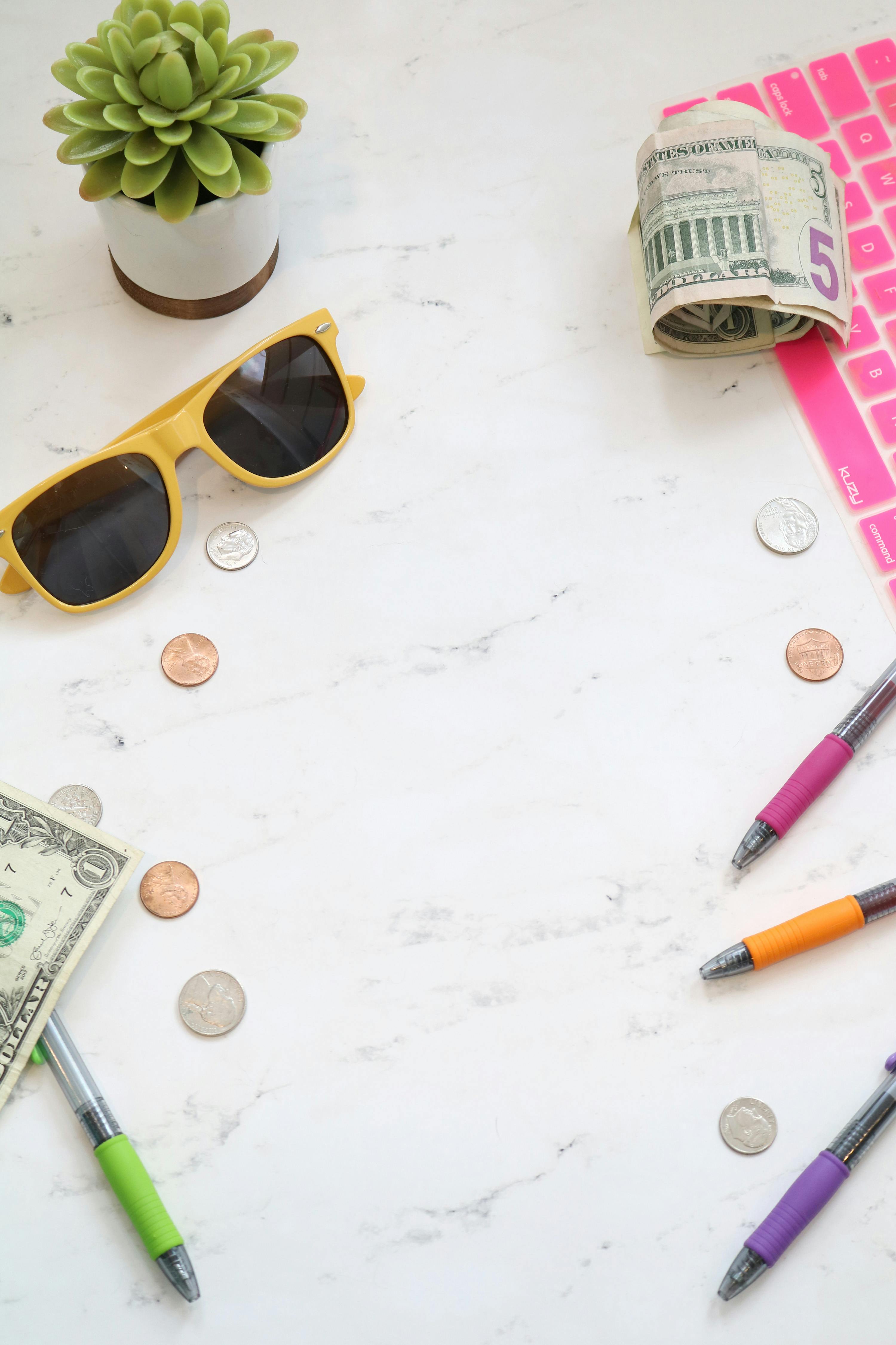 dollar bills coins succulent sunglasses and pens on marble surface