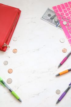 Flat lay of red wallet, coins, and colorful pens on a white desk with copy space.
