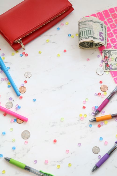 Free Flat lay of a creative workspace featuring currency, stationery, and colorful sequins on a marble surface. Stock Photo