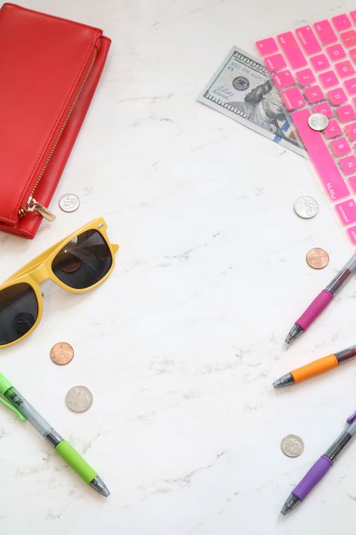 Sunglasses, a wallet, and coins arranged on a marble surface, representing the choice between travel rewards and cash back