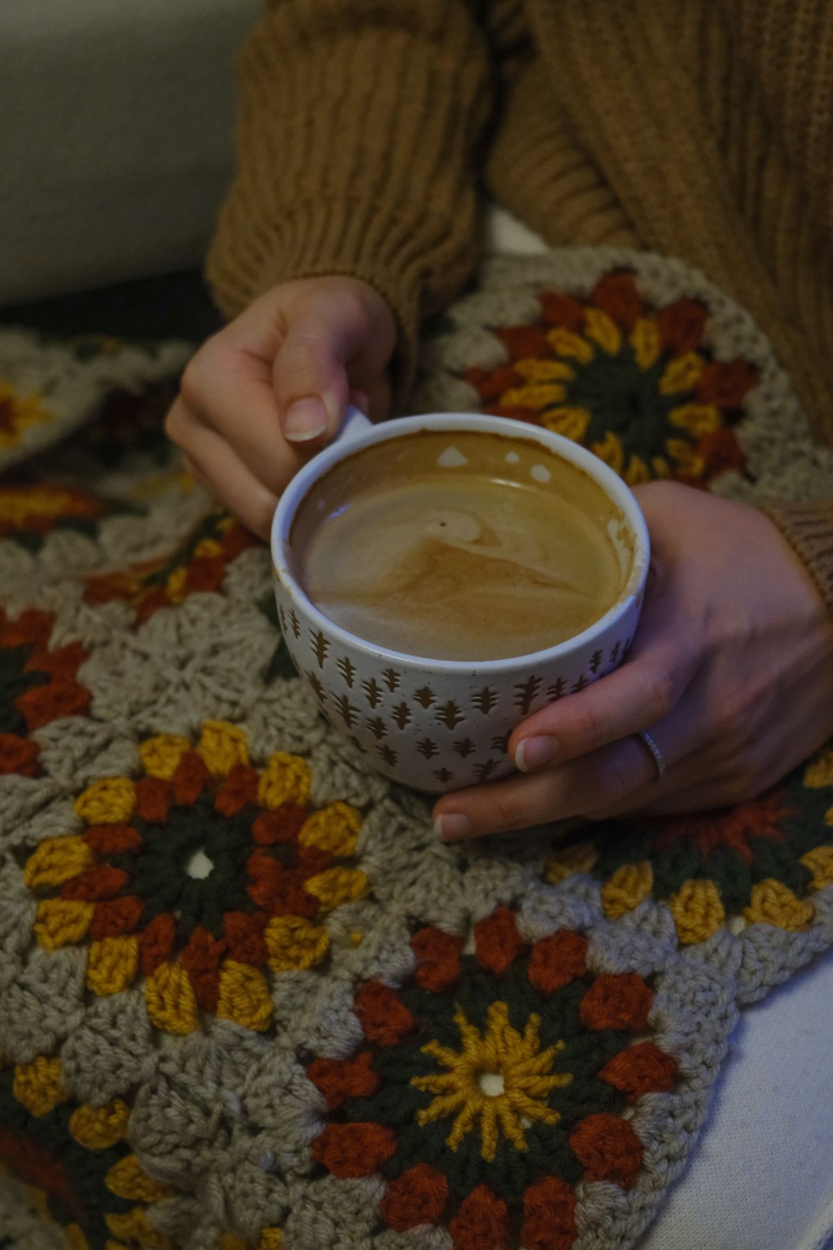 Woman holding coffee on a crocheted blanket, perfect for a cozy autumn morning.