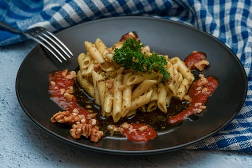 Photo of Italian penne, herbs, and a touch of tomato sauce on a Black plate.