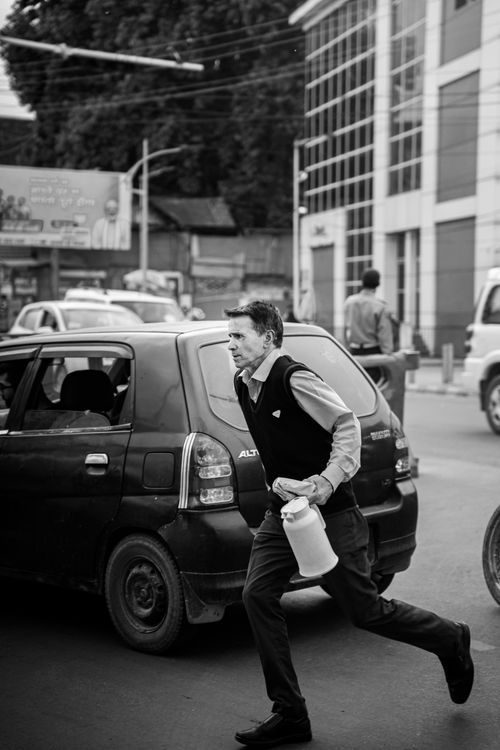 Free A man hurriedly crossing a busy street carrying a water jug in a city setting. Stock Photo