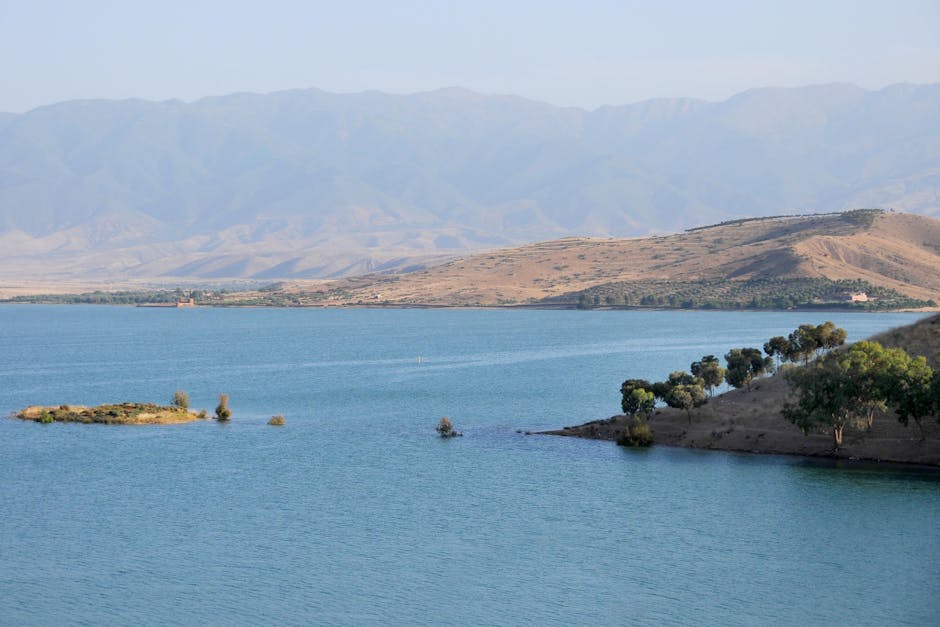 Tranquil view of Ouarzazate's lake with surrounding hills and distant mountains in Morocco.